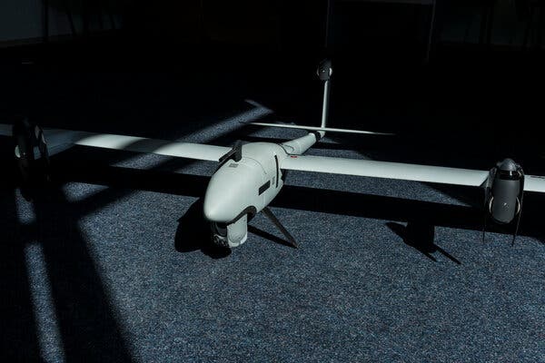 A drone built like a plane on a gray carpet, with some moody lighting in a room. 