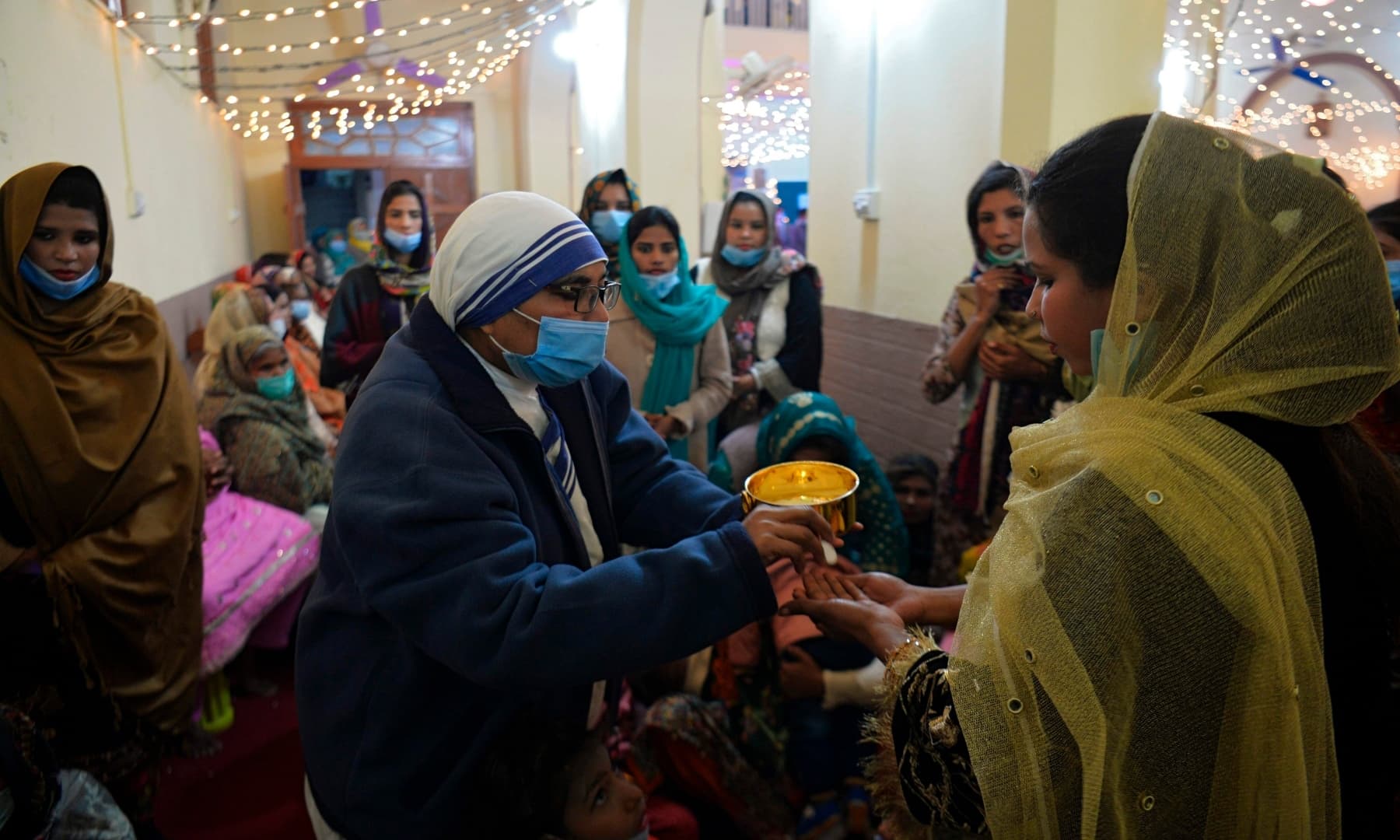 A nun wearing a facemask distributes holy communion to devotees during Christmas prayers at the Holy Family Catholic Church in Rawalpindi on December 25. — AFP