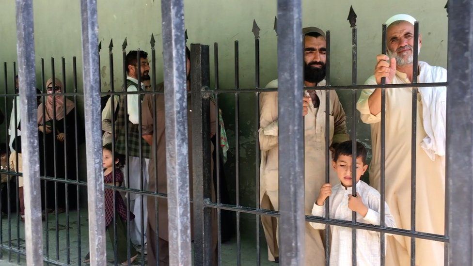 Afghans wait behind a fence to cross into Pakistan at Torkham