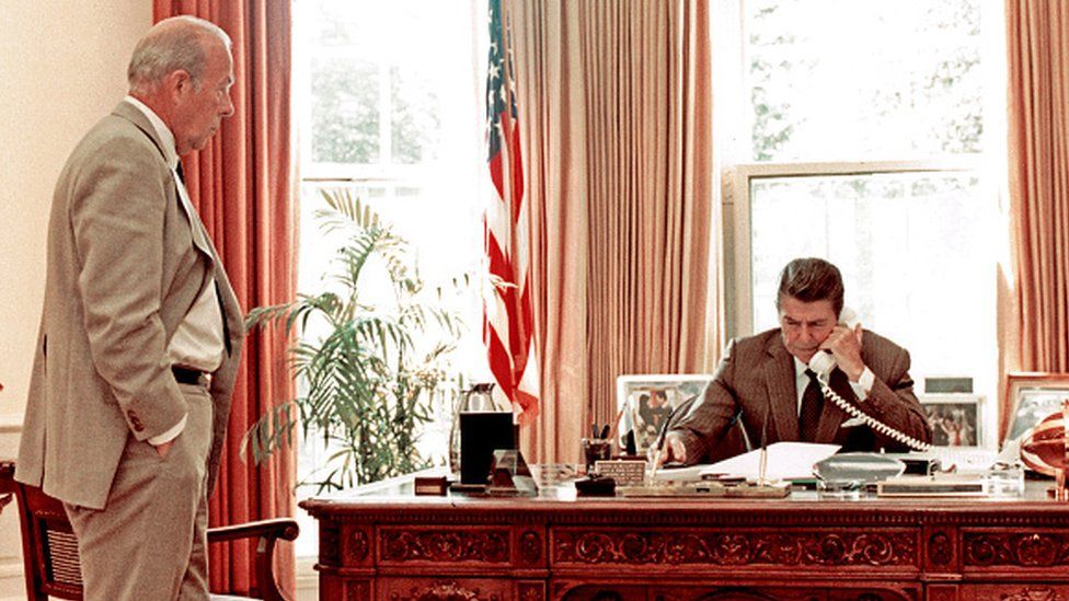 US Secretary of State George Shultz watches as US President Ronald Reagan speak on the phone