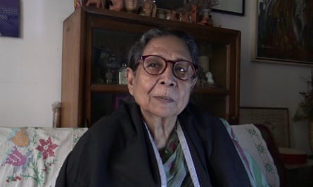 An older woman sitting on a sofa looks at the camera 
