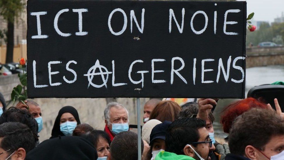 Placard saying: Here we drown Algerians seen at a remembrance ceremony to mark the 59th anniversary of the 1961 Paris massacre at the Pont Saint-Michel bridge over the River Seine in Paris, France - 17 October 2020