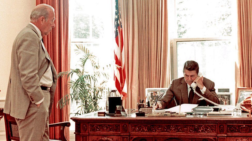 US Secretary of State George Shultz watches as US President Ronald Reagan speak on the phone US Secretary of State George Shultz watches as US President Ronald Reagan speak on the phone