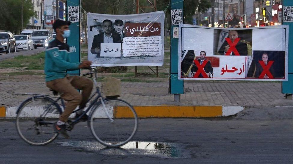 A man rides his bicycle past a banner in Karbala reading in Arabic Who killed me? and depicting renowned Iraqi anti-government activist Ehab al-Wazni, who was shot dead (23 May 2021)