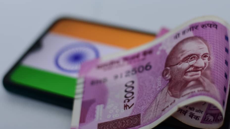 Two thousand rupee notes on display with an Indian flag in the background.