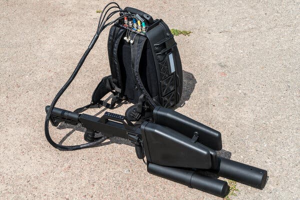 A plastic black drone device connected to a device in a back pack on the ground. 