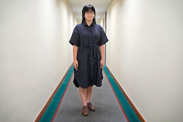 A woman in a blue striped dress stands in a hallway.