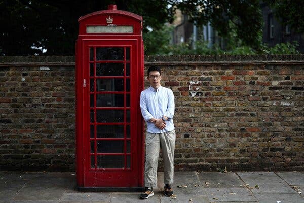 A man leans against a British-style red phone booth.